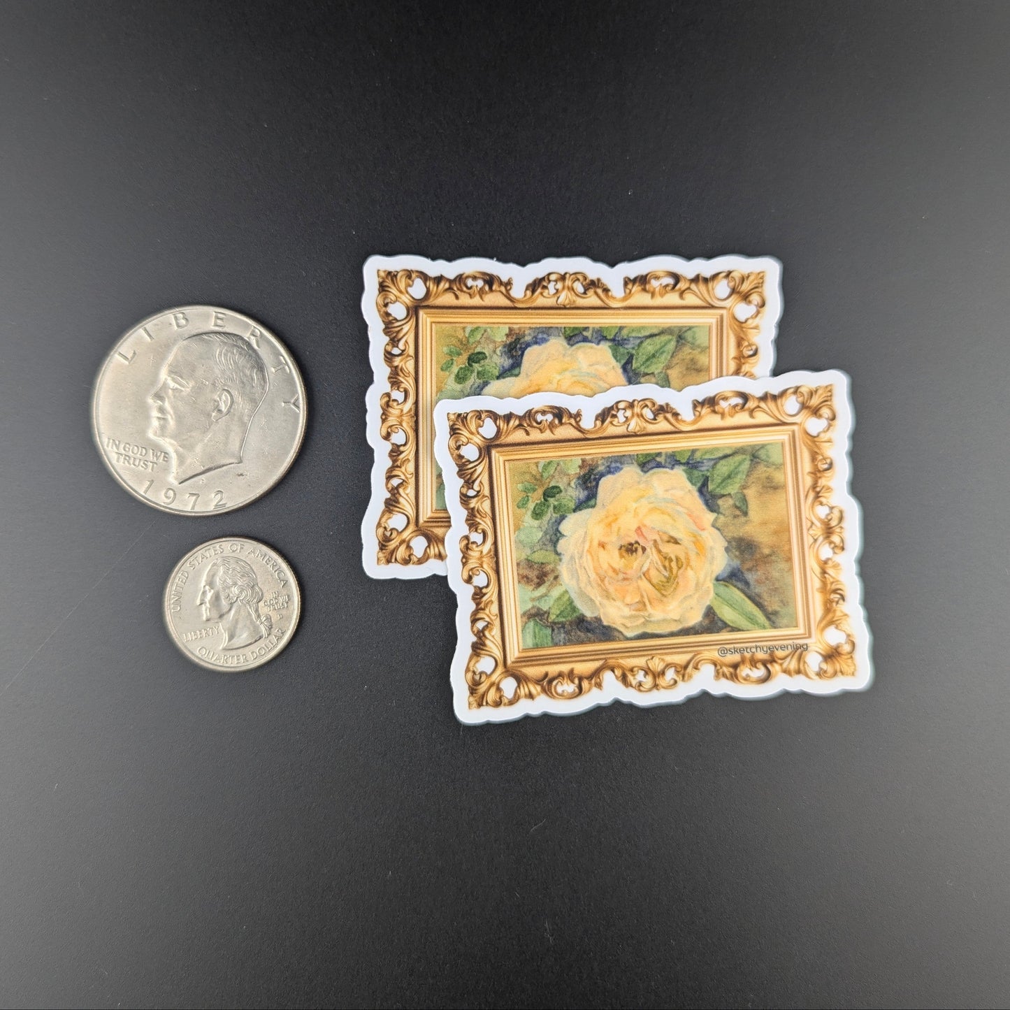 Two miniature framed artworks with a coin for scale on a dark background