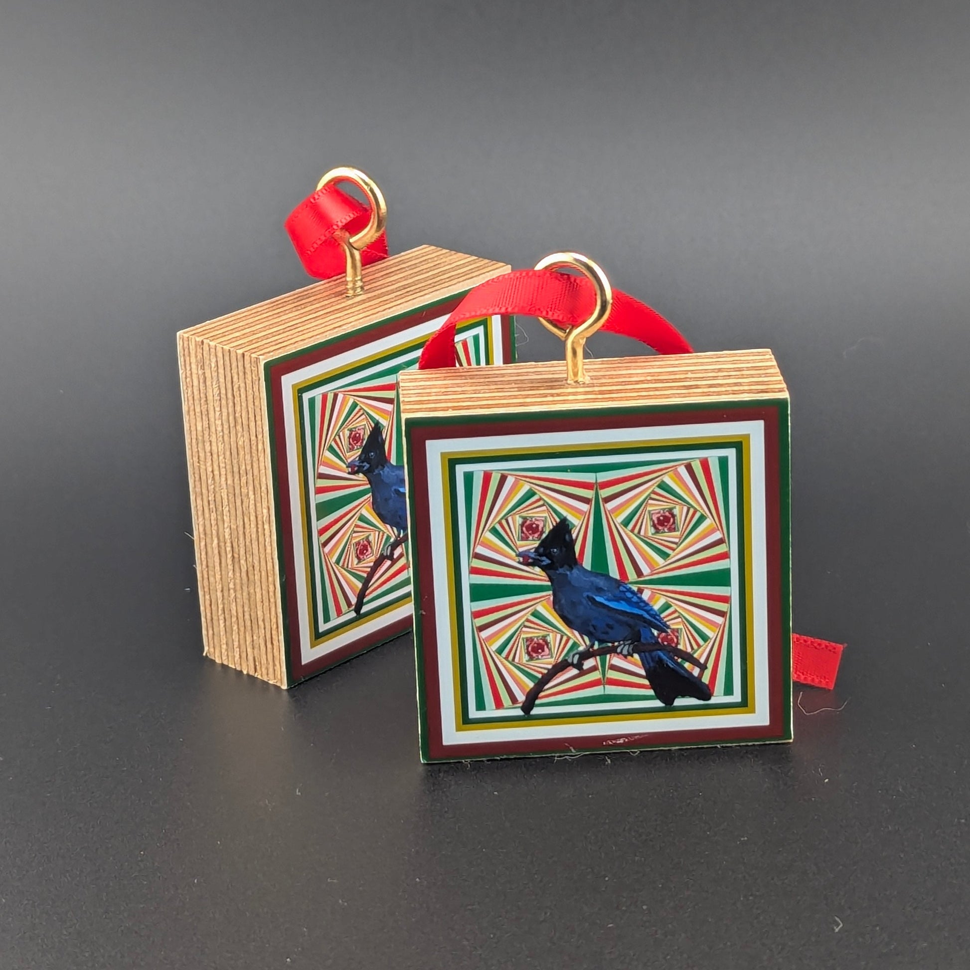 Two decorative and festive wooden ornament blocks with bird illustration with a geometric spiral background