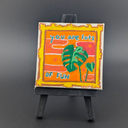 Small painted sign on a stand with 'You are lots of fun' text and a leaf illustration, against a dark background.