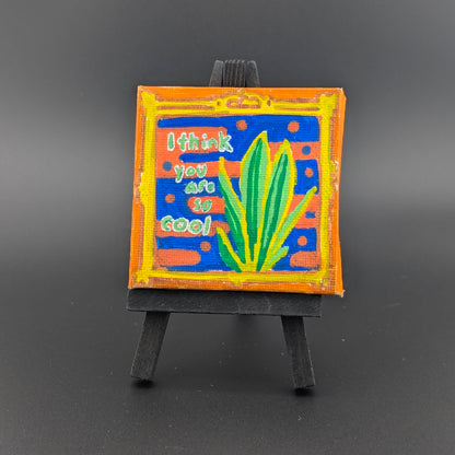 Small painting on an easel with text and abstract design against a dark background