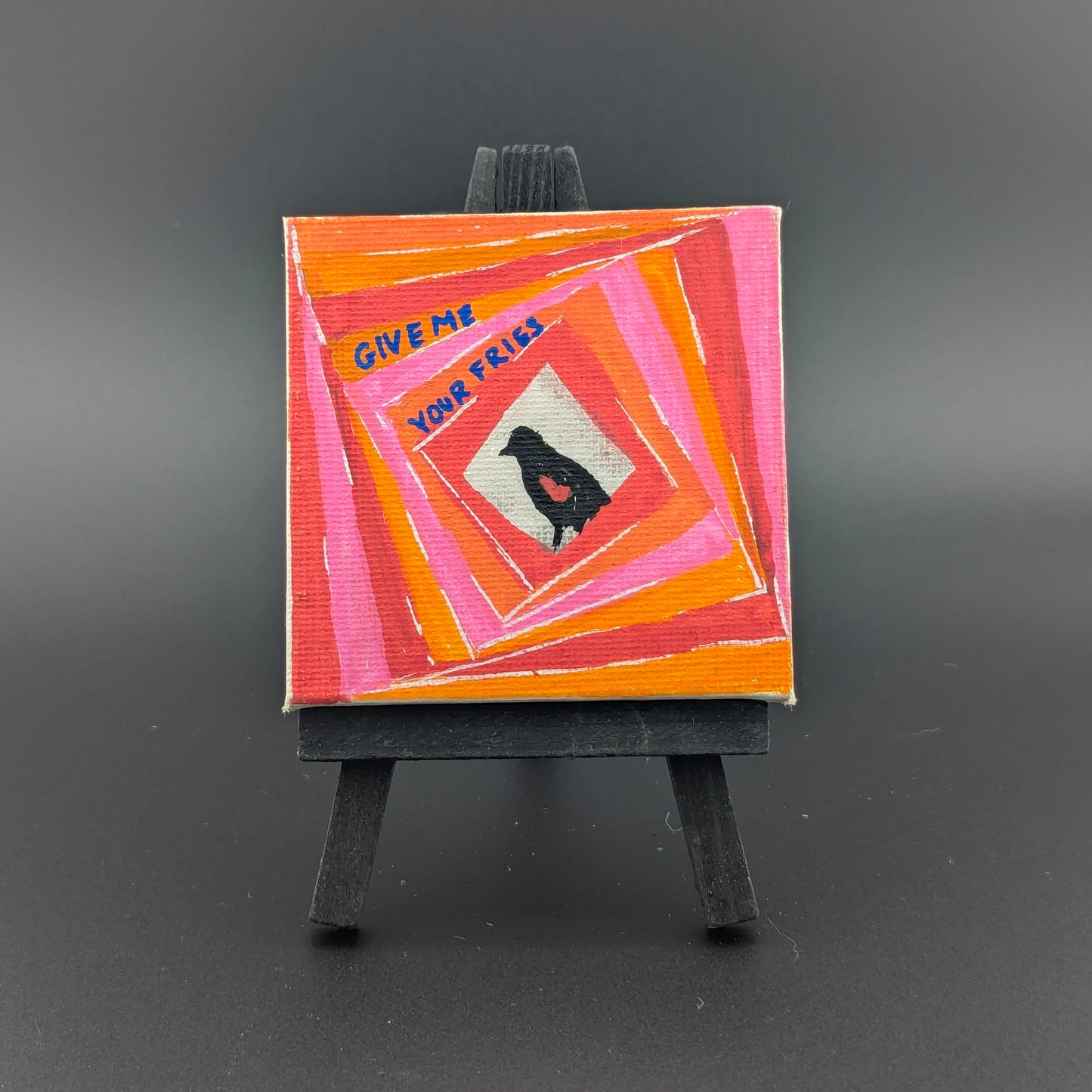 Small painting on an easel with a colorful abstract design and text on a dark background