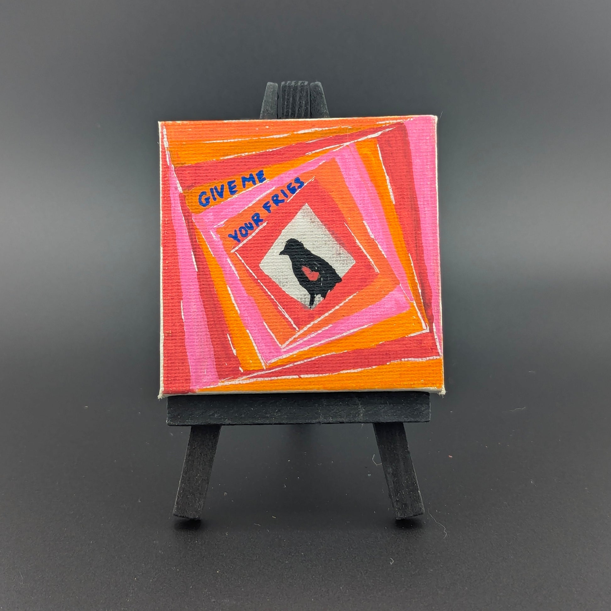 Small painting on an easel with a colorful abstract design and text on a dark background