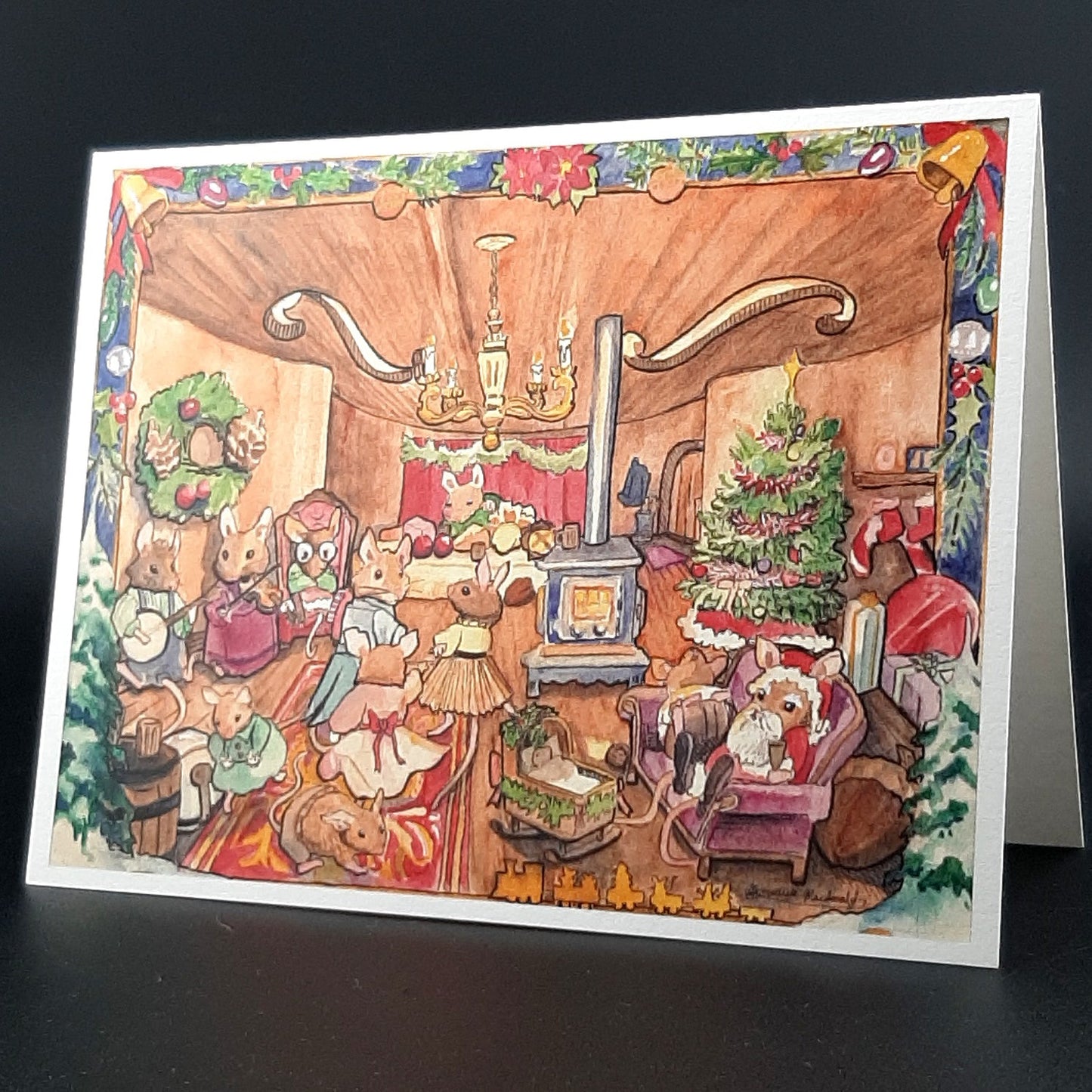 Illustrated Christmas card with a festive living room scene inside of a violin with dancing mice and santa and a wood stove on a black background
